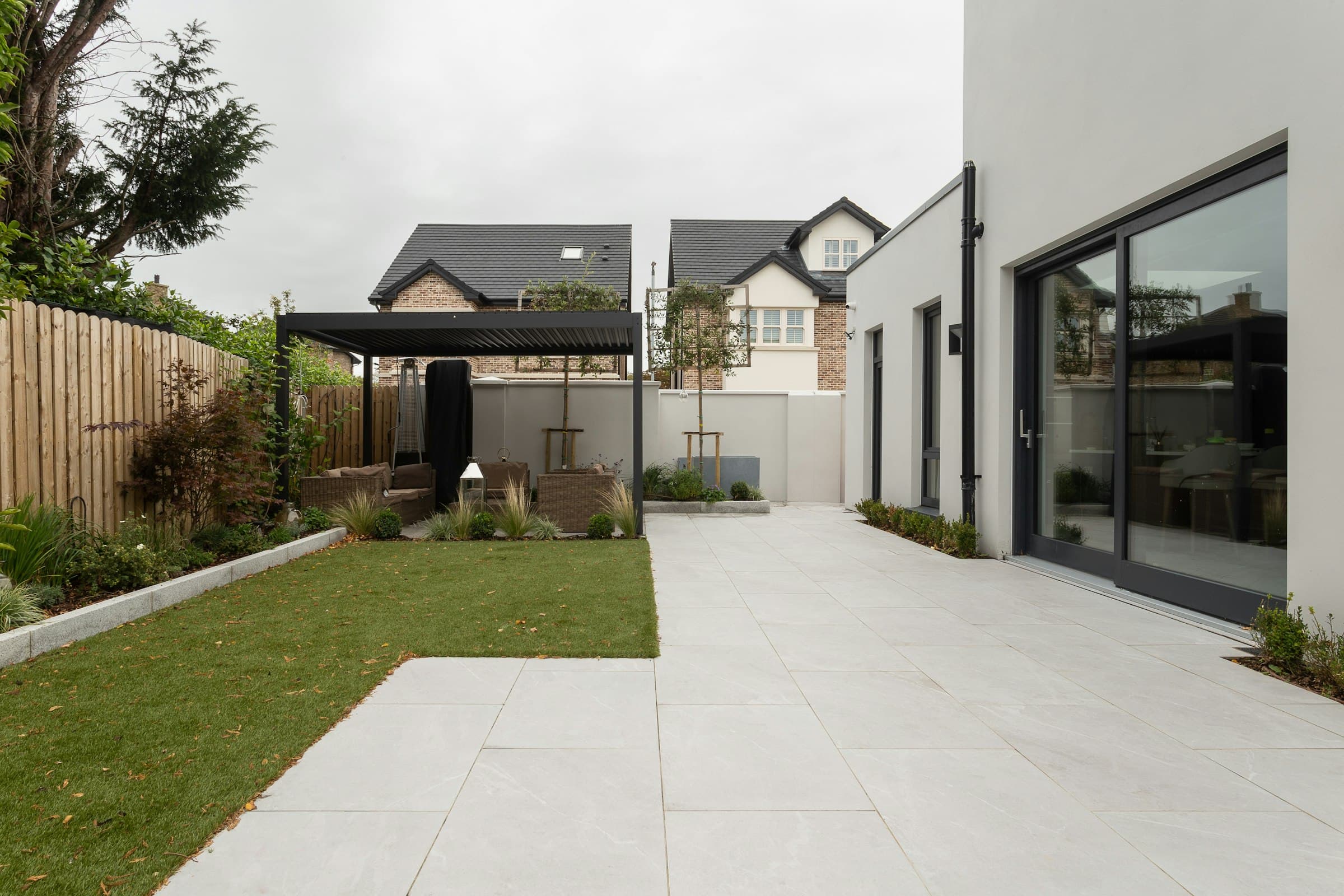 BEISPIEL-FOTO: moderner Hausgarten mit heller Steinterrasse, Rasen, Pergola und Holzzaun